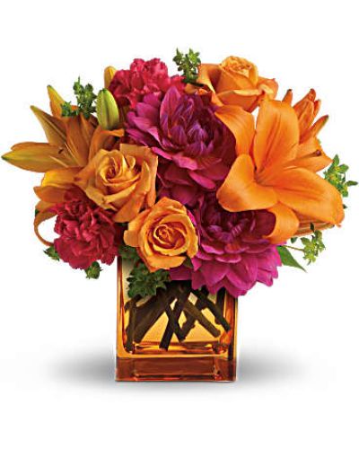 Feeling hot, hot, hot! This sizzling summer floral arrangement mixes hot pink dahlias and carnations with bright orange roses and lilies in an orange cube vase. It’s the floral equivalent of a trip to Miami in July!
Light orange roses, orange asiatic lilies, hot pink dahlias and hot pink carnations are presented with fresh green bupleurum in an orange glass cube vase.