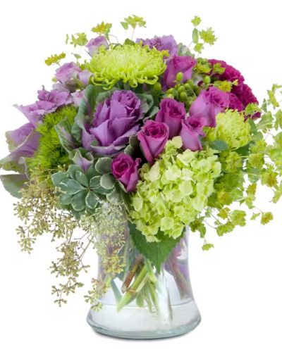 A magical mixture of magenta and green flowers, including roses, hydrangea, hypericum berry and ornamental kale, designed in a large clear glass vase.